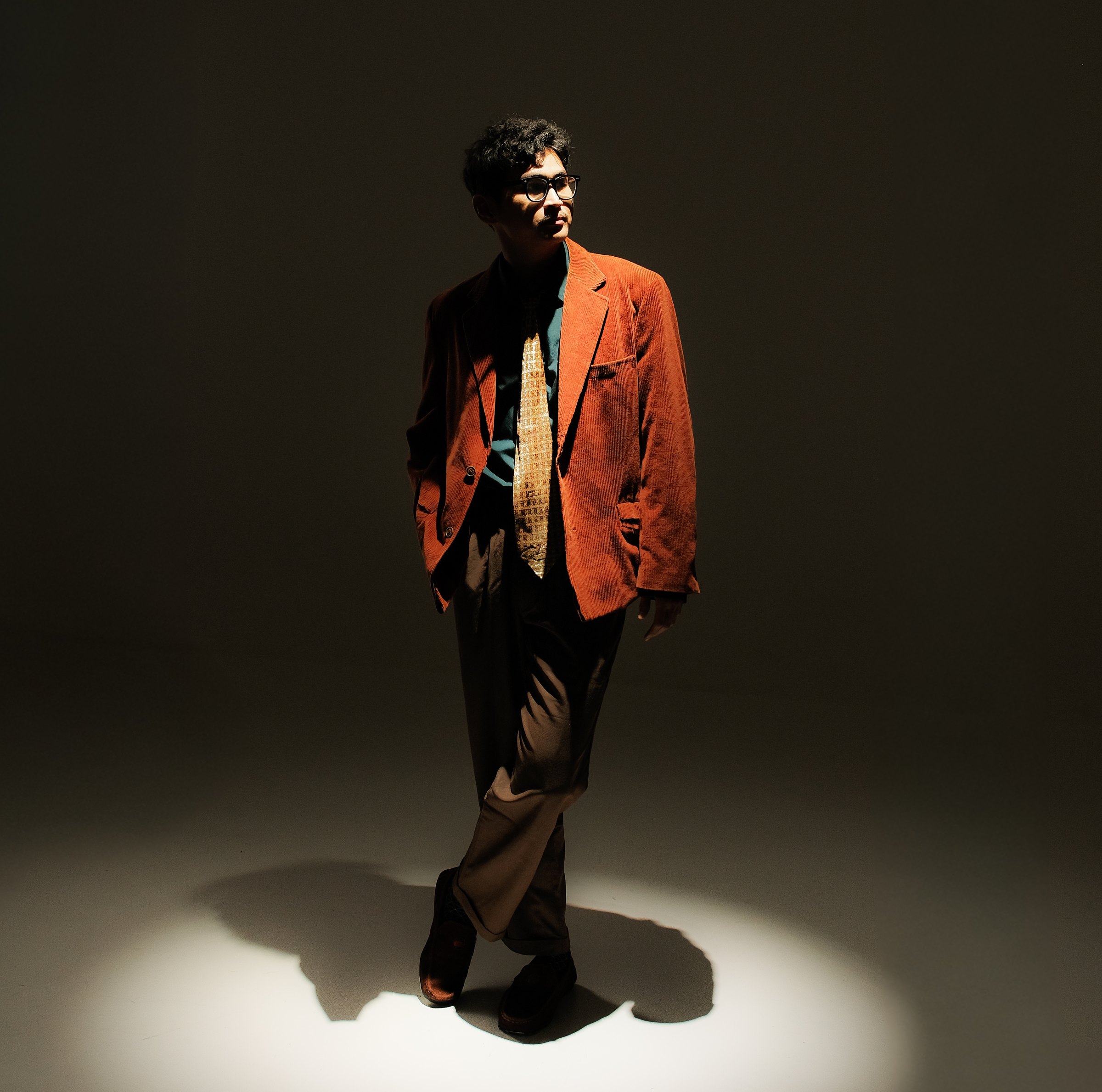 Billy Endson standing under a stage spotlight wearing an orange jacket